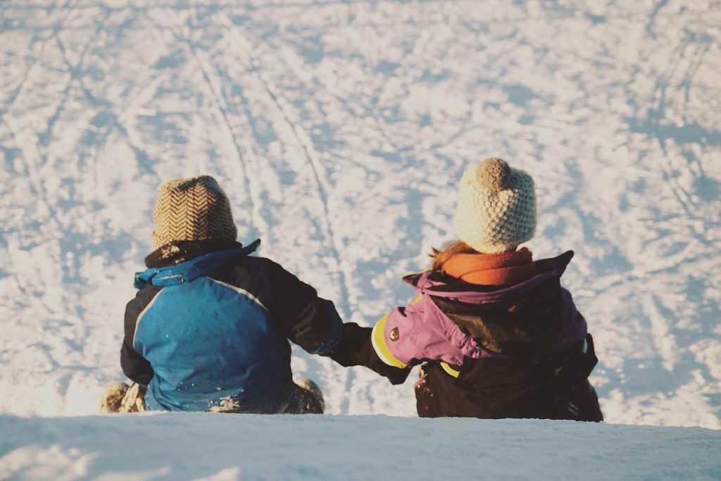 Two Kids holding hands while sledding in a sno park near Fresno